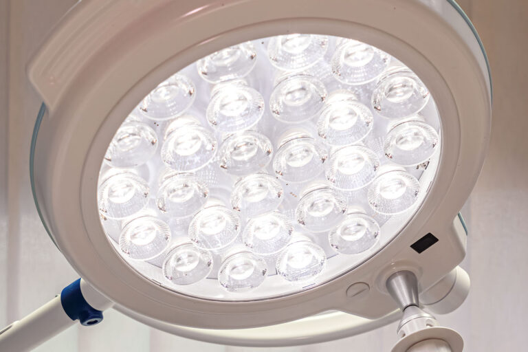 Nahaufnahme einer hellen OP-Lampe mit mehreren runden LED-Lichtern in einer kreisförmigen Anordnung. Die Lampe ist Teil eines medizinischen Geräts und dient der Ausleuchtung von Operationsbereichen.